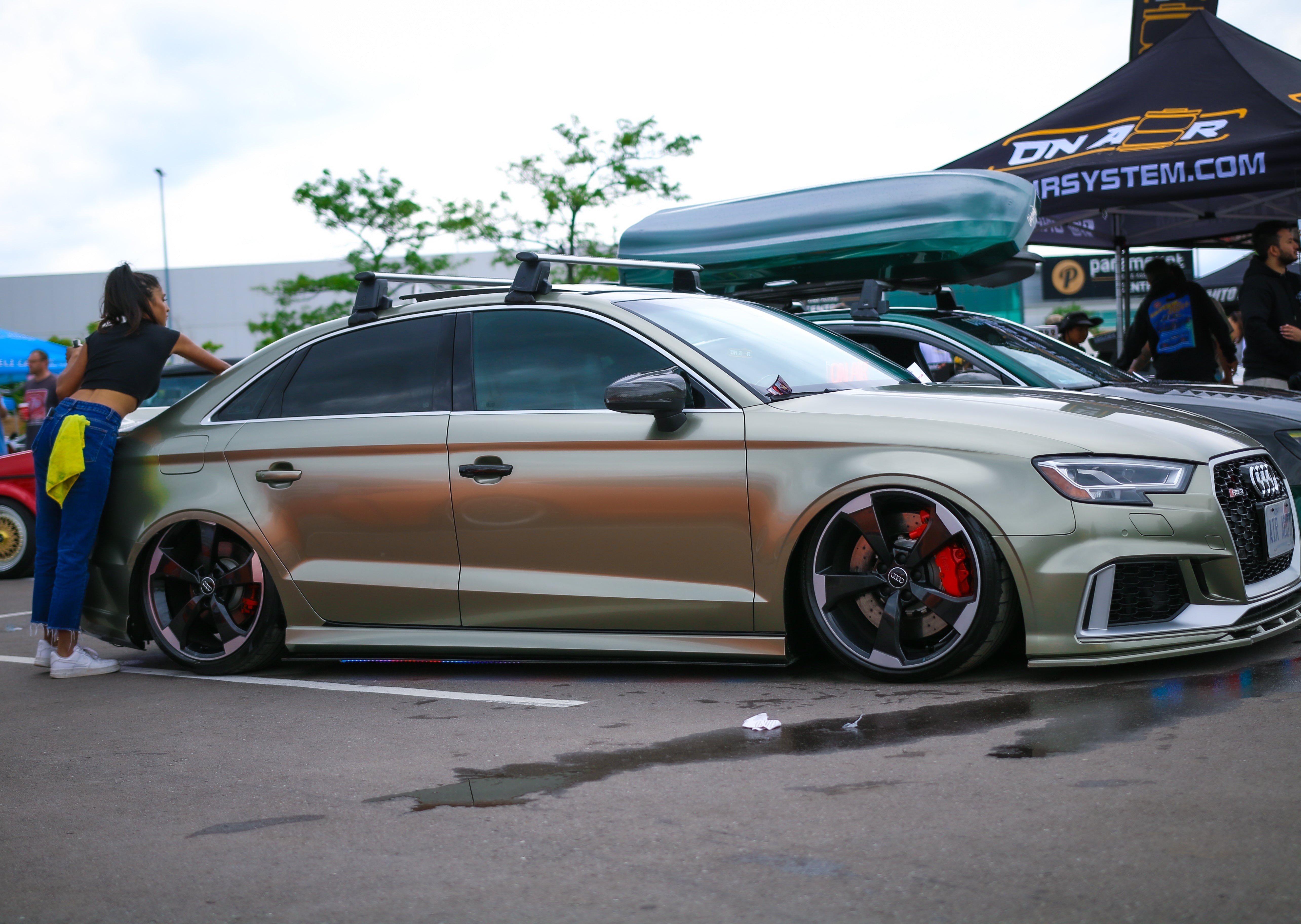 Image of Air Audi rs3 beside Zayns S3, Safia cleaning the back of the rs3 with a yellow microfiber towel in her back pocket. showing a clear side shot of the audi